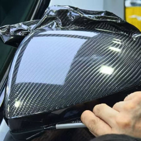 A person applies Carbon Fiber Carbon SelfRepair Nano-Coated PPF to a car’s side mirror, carefully smoothing the protective film over the surface with their hand.