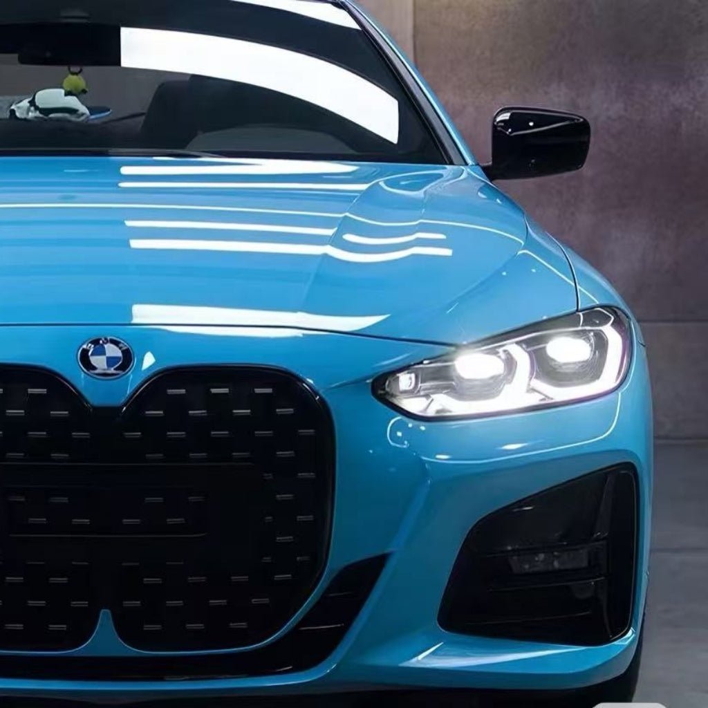 Close-up front view of a blue BMW with glowing right headlight, kidney grille, plush toy on windshield—protected by Sky Blue Charm SelfRepair Nano-Coated PPF for maximálna ochrana karosérie.