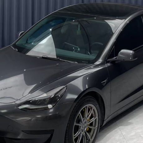 A sleek, dark grey Tesla Model 3 in Diamond Coal Gray Glossy SelfRepair Nano-Coated PPF is parked indoors on a shiny floor with a dark curtain backdrop. The futuristic design, tinted windows, and advanced protective PPF film stand out.
