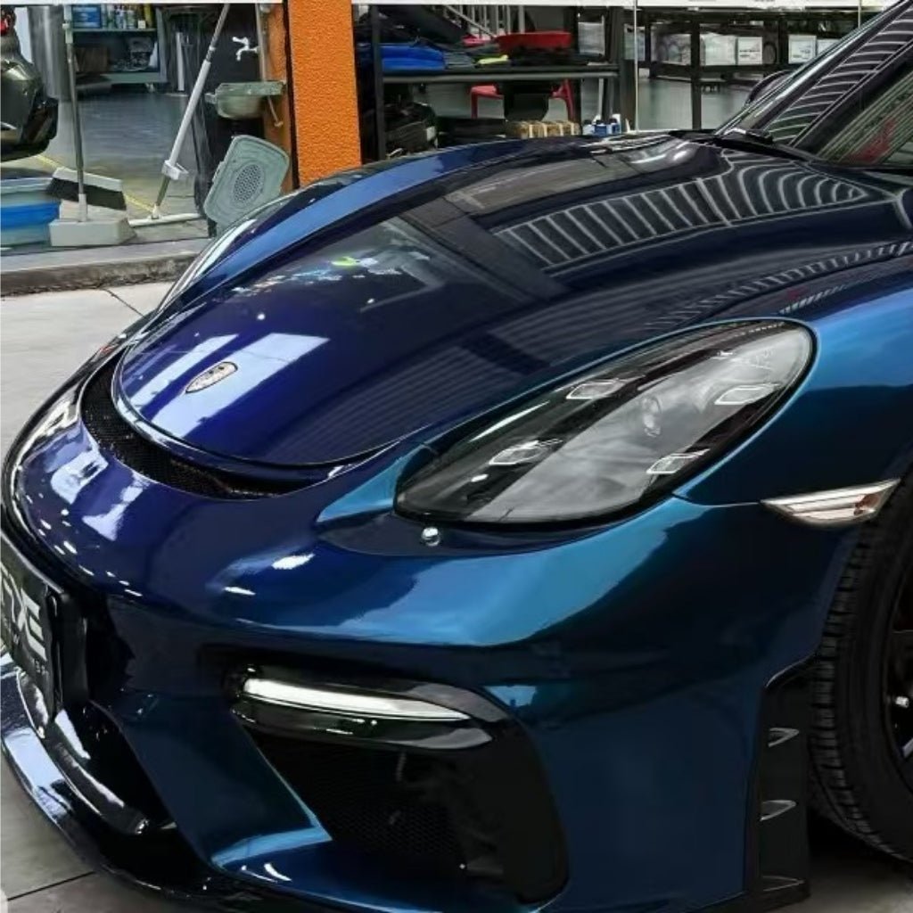 Close-up of a shiny dark blue sports car front, protected by Diamond Dark Shadow Blue Glossy SelfRepair Nano-Coated PPF, parked indoors with reflections on the hood and windshield highlighting the premium film.