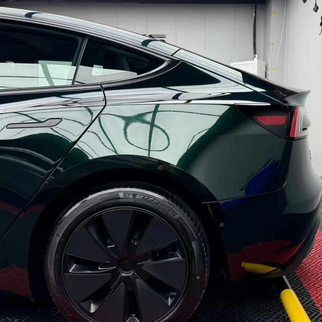 A close-up of the rear side of a shiny black car showcases the Diamond Emerald Glossy SelfRepair Nano-Coated PPF, highlighting its self-repair finish on the back wheel, tinted windows, and sleek curves reflecting lights in an indoor garage.
