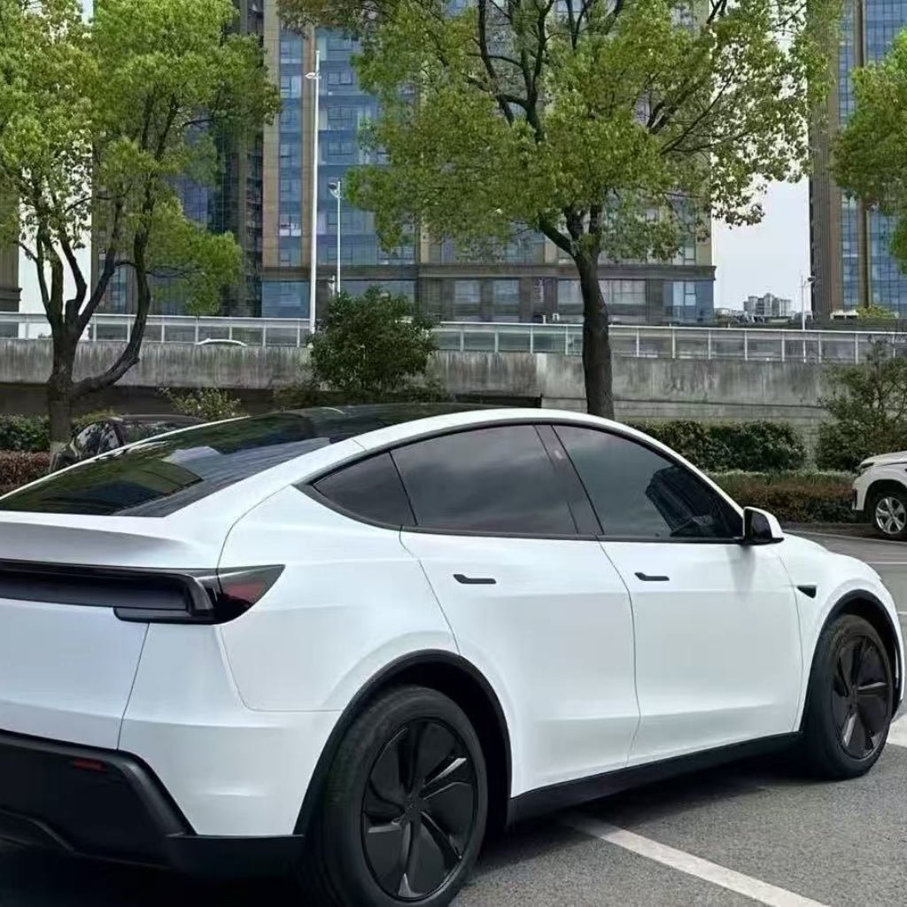 A white Tesla Model Y protected with White Diamond Glossy SelfRepair Nano-Coated PPF is parked in a lot near trees and modern glass buildings on a clear day.