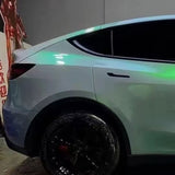 A shiny white car with black wheels is parked indoors. Green light reflects off the rear side, including back door and tire, thanks to the ochrana karosérie of Gray to Green Charm Glossy SelfRepair Nano-Coated PPF.