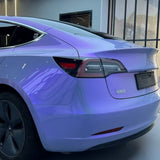 A close-up of a Tesla Model 3 featuring Gray to Purple Charm Glossy SelfRepair Nano-Coated PPF, parked indoors. The taillight, rear window, and black wheels are prominent; Chinese characters appear on the trunk.