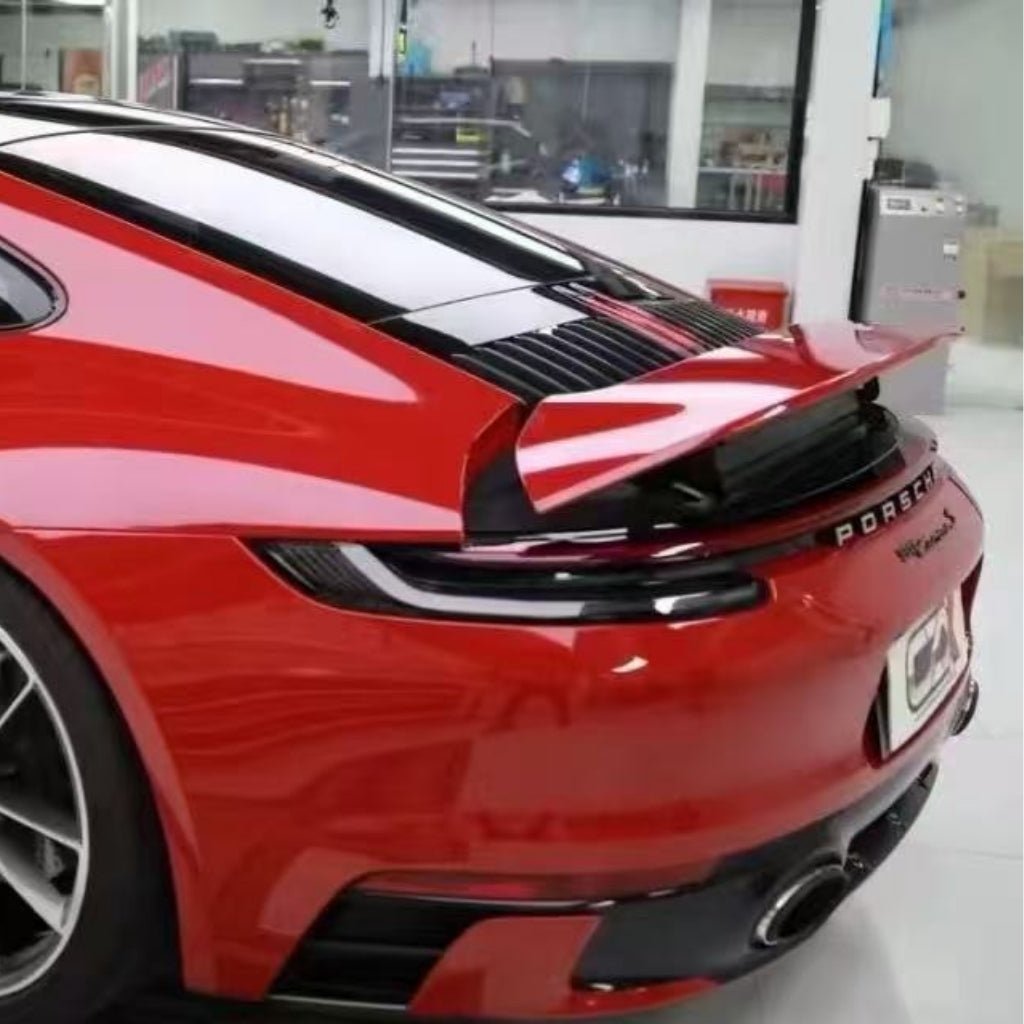 A close-up of the rear end of a red Porsche sports car with Fire Red Laser SelfRepair Nano-Coated PPF, highlighting its raised rear spoiler, sleek taillights, and dual exhausts in a modern garage.