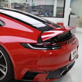A close-up of the rear end of a red Porsche sports car with Fire Red Laser SelfRepair Nano-Coated PPF, highlighting its raised rear spoiler, sleek taillights, and dual exhausts in a modern garage.