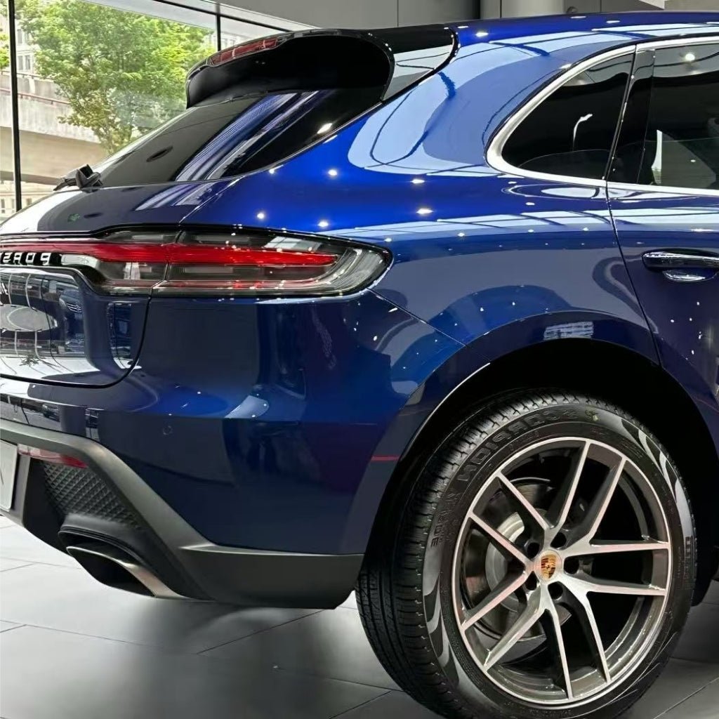 A close-up of the rear side of a blue Porsche SUV indoors showcases the back wheel, taillight, and rear windshield, finished with Diamond Gentian Blue Glossy SelfRepair Nano-Coated PPF reflecting indoor lights.