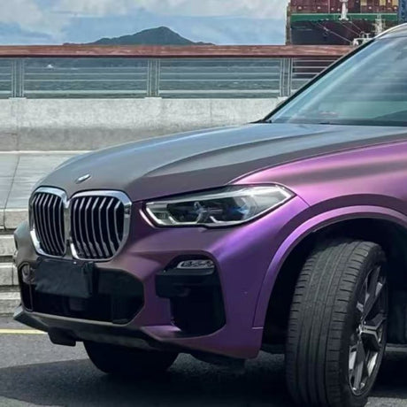 A purple BMW SUV with Gold White Red Chameleon SelfRepair Nano-Coated PPF is parked by a waterfront with a ship and mountains, highlighting its front side, unique finish, and nano-coated ochranná fólia na auto.