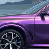 A BMW featuring Gold White Red Chameleon SelfRepair Nano-Coated PPF is parked by the water, its front side, wheel, and part of the windshield highlighted against a scenic mountain and water backdrop.