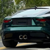 A close-up of the rear end of a dark green Jaguar F-Type in Diamond British Green Glossy SelfRepair Nano-Coated PPF, highlighting dual exhaust pipes, taillights, and a blank license plate area with trees in the background.