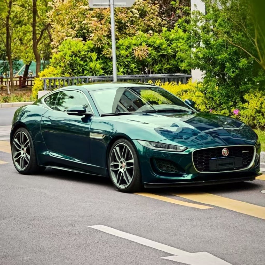 A Jaguar sports car with Diamond British Green Glossy SelfRepair Nano-Coated PPF is parked on a city street, surrounded by lush green trees and bushes, on a bright day.