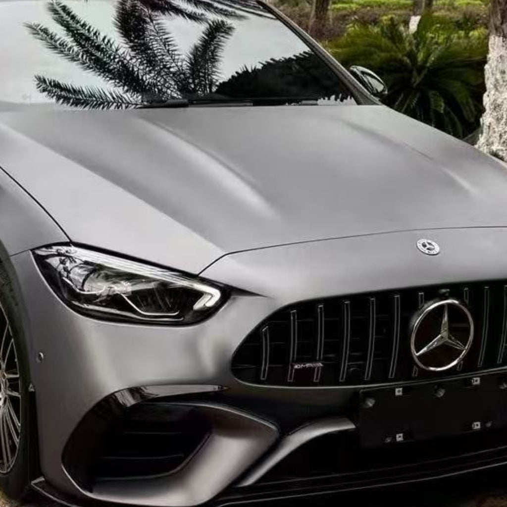 A close-up of a Mercedes-Benz front in AMG Mountain Gray Matte SelfRepair Nano-Coated PPF, showcasing the grille, emblem, sleek headlights, and palm tree reflections—all safeguarded by advanced self-healing nano technology.