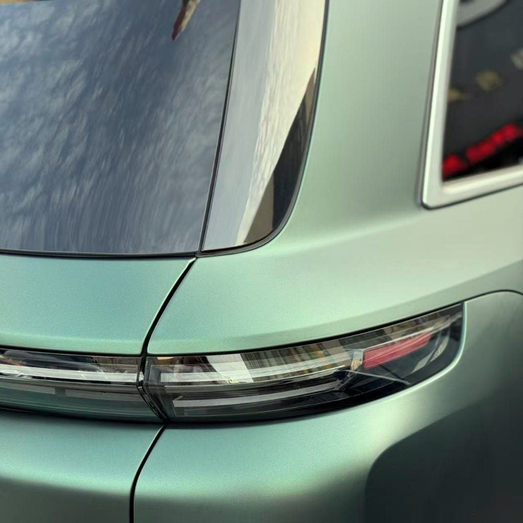 Close-up of a mint green car’s rear corner, featuring a sleek taillight and rear window, enhanced by Dark Green Matte SelfRepair Nano-Coated PPF for protection and a stylish look, with sky reflections visible above.