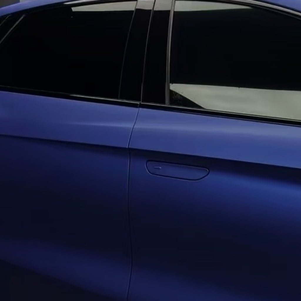 A close-up view of a dark blue car’s side showcases the rear passenger door wrapped in Diamond Blue Matte SelfRepair Nano-Coated PPF and tinted windows under soft lighting.