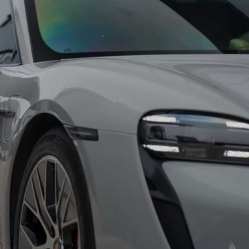 Close-up of the front left side of a silver car with Porsche Gray Matte SelfRepair Nano-Coated PPF, highlighting the wheel, headlight, and part of the windshield with a rainbow reflection from the matte protective film.