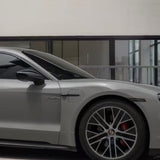 A sleek silver sports car, viewed indoors by large glass windows, showcases its front wheel and door enhanced with Porsche Gray Matte SelfRepair Nano-Coated PPF for modern design and advanced self-healing protection.