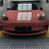 A front view of a pink Tesla Model 3 in Morganite Red Glossy SelfRepair Nano-Coated PPF, parked indoors as ceiling grid windows reflect on its hood, highlighting advanced body protection and self-healing nano technology.