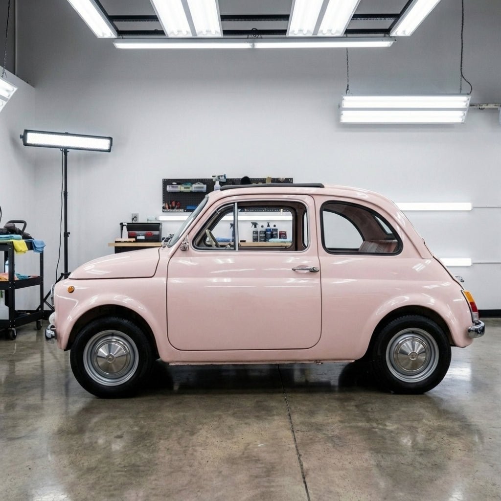 A classic Pearl Blossom Pink compact car is parked indoors under bright lights in a clean garage, protected by Nexthor™ Pearl Blossom Pink Glossy SelfRepair Nano-Coated PPF.