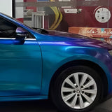 A shiny car with Purple Blue Green Chameleon SelfRepair Nano-Coated PPF is parked indoors, showcasing its front and wheel. Behind it, a colorful mural with a banana, text, and graphics adds vibrant flair.