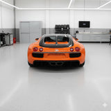An orange Bugatti featuring Diamond Racing Orange Glossy SelfRepair Nano-Coated Nexthor™ PPF is parked in a modern garage with gray cabinets, workbenches, and a wall-mounted TV in the background.