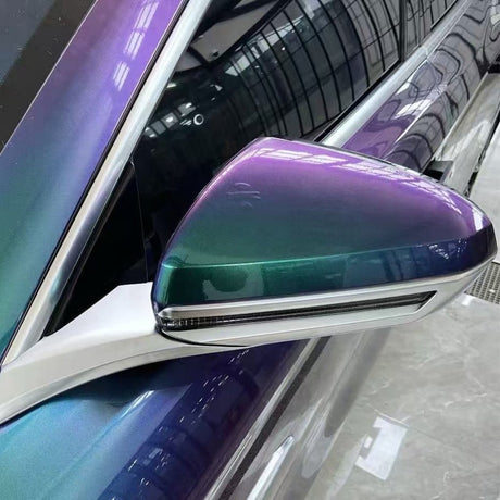 A close-up of a car's side mirror shows the Red Blue Green Chameleon SelfRepair Nano-Coated PPF, its glossy finish shifting colors from green to purple and reflecting indoor lights and ceiling structure.