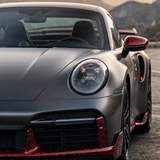 Close-up of a silver sports car featuring Red Forged Carbon Graphite Self-Healing Nano-Coated PPF and red accents, parked on a winding mountain road at sunset, showcasing its modern headlights and carbon fiber finish.