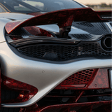 Close-up of the rear end of a silver and red sports car, highlighting its aerodynamic spoiler, sleek curves, mesh grille, and Red Forged Carbon Graphite Self-Healing Nano-Coated PPF with a carbon fiber finish gleaming in sunlight.