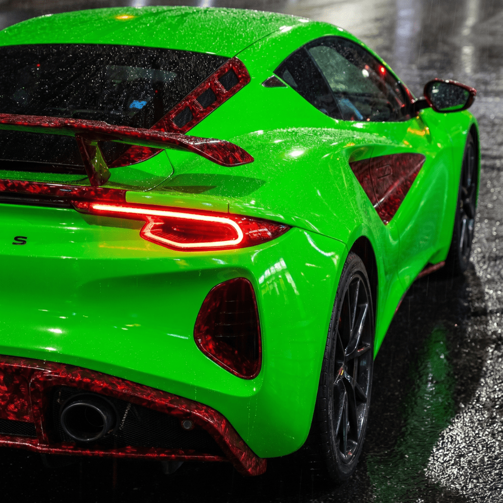 A sports car with red forged carbon graphite self-healing nano-coated PPF is parked on a wet street at night, illuminated by streetlights reflecting off the rain-soaked surface.