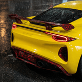 A yellow sports car with Red Forged Carbon Graphite Self-Healing Nano-Coated PPF is parked on a wet street at night, rain droplets sparkling on its surface, and red accents highlighting the rear spoiler and bumper.