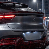 A close-up of the rear of a dark Ferrari SUV at night shows glowing red tail lights and rain droplets on a Red Forged Carbon Graphite Self-Healing Nano-Coated PPF surface, with 'NEXTHOR' displayed below the Ferrari emblem.