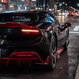 A sleek black supercar with red accents and a Red Forged Carbon Graphite Self-Healing Nano-Coated PPF is parked on a city street at night, illuminated by streetlights. Its glowing rear lights emphasize the modern design.