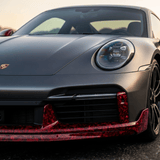 Close-up of a Porsche front end with a Red Forged Carbon Graphite Self-Healing Nano-Coated PPF, showing the matte black finish, left headlight, hood emblem, and a front bumper highlighted by a distinctive red accent.