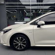 A car protected with Satin Liquid Metallic Bronze SelfRepair Nano-Coated PPF, featuring black alloy wheels, is parked indoors under ceiling lights. The front door, mirror, and hood are visible with a glass wall and another vehicle in the background.