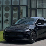 A sleek black Tesla with Shell Black Glossy SelfRepair Nano-Coated PPF is parked on a street before a modern building featuring large glass windows and doors decorated with circular patterns.