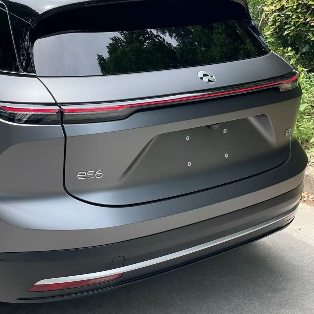 The rear view of a gray Nio ES6 electric SUV parked near greenery, featuring taillights spanning the back and an es6 badge on the left, protected by Silver Liquid Metallic Matte SelfRepair Nano-Coated PPF for karoséria protection.