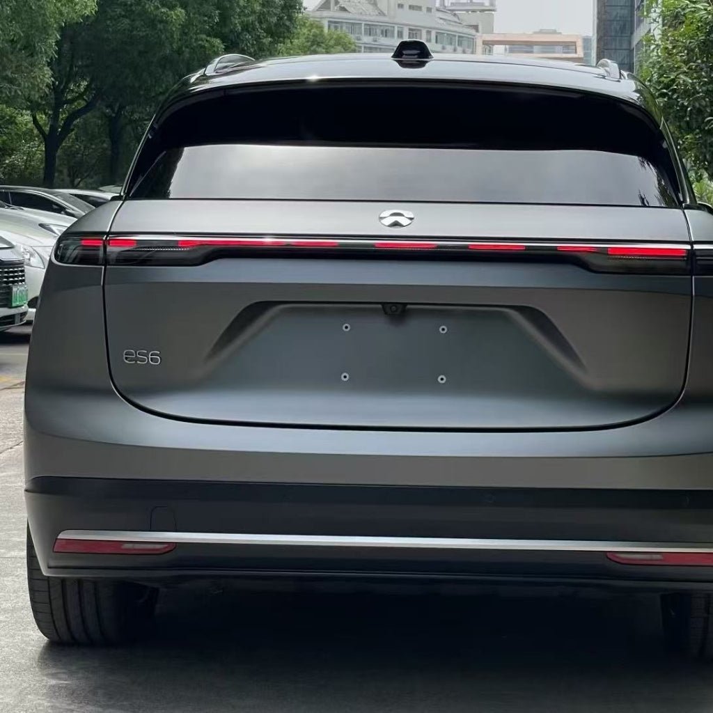 Rear view of a grey NIO ES6 electric SUV with sleek design and horizontal taillight bar, featuring Silver Liquid Metallic Matte SelfRepair Nano-Coated PPF for body protection. Trees and parked cars are visible in the background.