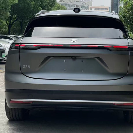 Rear view of a grey NIO ES6 electric SUV with sleek design and horizontal taillight bar, featuring Silver Liquid Metallic Matte SelfRepair Nano-Coated PPF for body protection. Trees and parked cars are visible in the background.