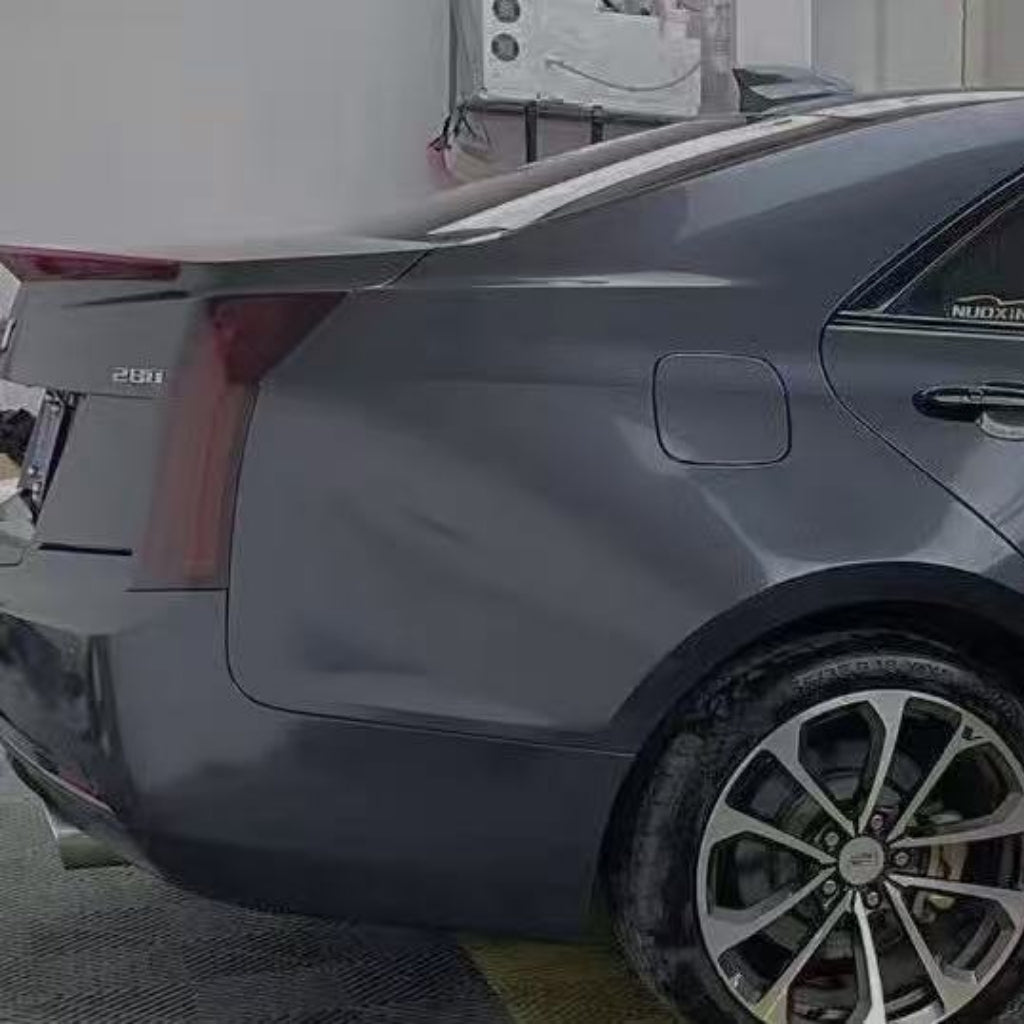 A close-up side view of a sedan's rear section features the Sparkle Black Matte SelfRepair Nano-Coated Nexthor™ film, highlighting the taillight, fuel door, rear wheel, and trunk while parked indoors.