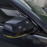 A close-up of a metallic gray car’s side mirror shielded by Sparkle Black Matte SelfRepair Nano-Coated Nexthor™ PPF and a partially open window, with reflections on its shiny surface and a softly blurred indoor background.