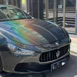 A black Maserati with a shimmering, rainbow-reflective hood featuring Stellar Black Glossy SelfRepair Nano-Coated PPF is parked on the street in front of a modern building with glass doors.