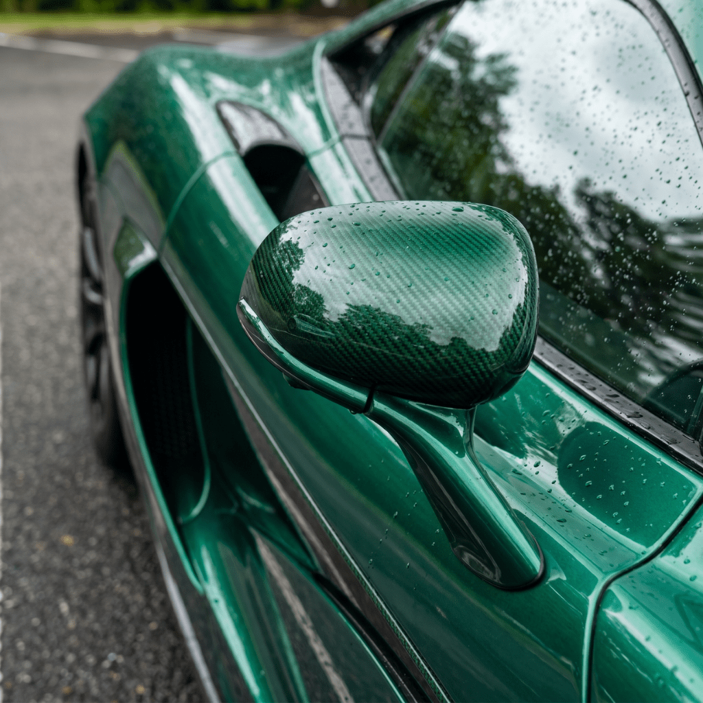 Close-up of a green sports car’s side mirror and door with raindrops, reflecting trees and sky. Surfaces are protected by Transparent Carbon Fiber Self-Healing Nano-Coated PPF for a sleek, glossy finish.