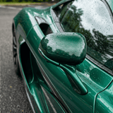Close-up of a green sports car’s side mirror and door with raindrops, reflecting trees and sky. Surfaces are protected by Transparent Carbon Fiber Self-Healing Nano-Coated PPF for a sleek, glossy finish.
