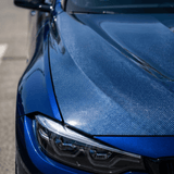 Close-up of a shiny blue car’s front section with Transparent Carbon Fiber Self-Healing Nano-Coated PPF on the hood, highlighting advanced surface protection and showing detailed headlight and hood design while parked on the street.