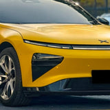 Close-up of the front of a modern electric car wrapped in Racing Yellow Glossy SelfRepair Nano-Coated PPF, featuring sleek narrow headlights and black trim. The vehicle is parked outdoors with its license plate blurred.