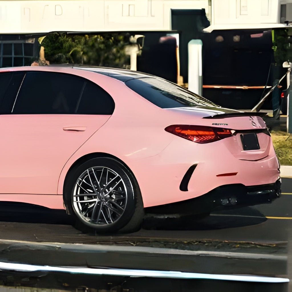 A pink Mercedes-Benz sedan with sporty alloy wheels and dark tinted windows, protected by Rouge Pink Glossy SelfRepair Nano-Coated PPF, is parked on the street against a blurred urban background.