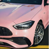 Close-up of the front left side of a shiny Rouge Pink Glossy SelfRepair Nano-Coated PPF car, with a modern headlight and silver alloy wheel, serving as an ochranná bariéra vozidla, parked beside a yellow road line.