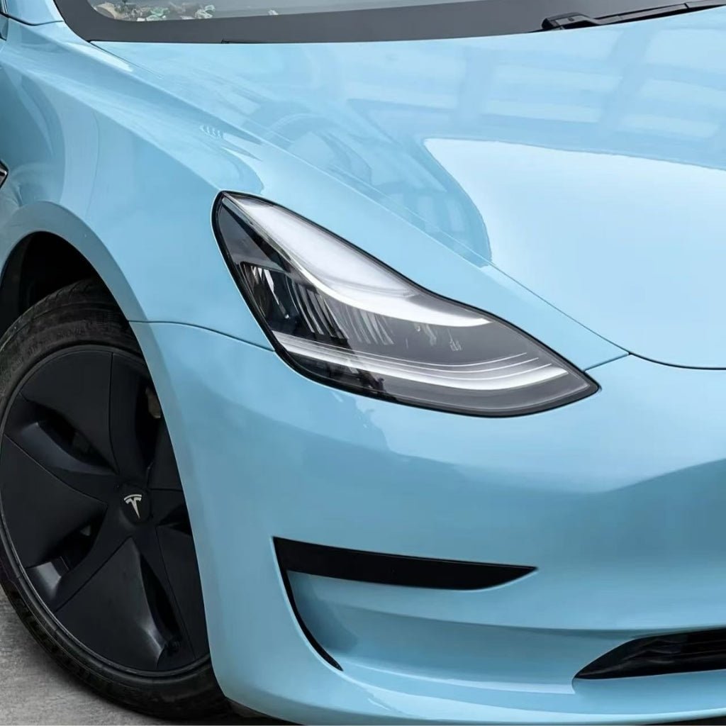 Close-up of the front left side of a light blue Tesla with a shiny finish protected by Sea Breeze Blue Glossy SelfRepair Nano-Coated PPF, highlighting its sleek headlight, black Tesla wheel, and advanced self-repair technology.
