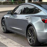 A silver Tesla Model 3, protected by Polar Titanium Liquid Metallic Glossy SelfRepair Nano-Coated PPF, is parked on the street near a sidewalk and shown from the rear side angle on a sunny day.