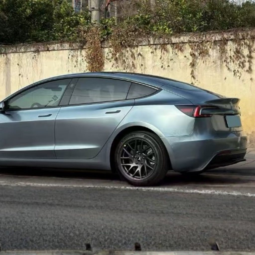 A metallic gray electric car with Polar Titanium Liquid Metallic Glossy SelfRepair Nano-Coated PPF is parked by a weathered yellow wall draped in vines. The self-healing PPF protects its sleek side and rear.