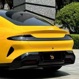 The rear view of a sports car in Sunshine Yellow Glossy SelfRepair Nano-Coated PPF, with sleek tail lights and a glossy black bumper, parked outdoors near greenery and a stone wall.